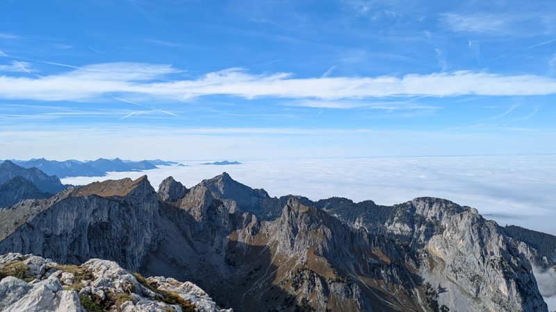 Vom Gipfel auf felsige Gratzüge, dahinter das Nebelmeer