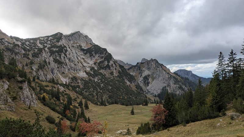 Almmulde mit Blick auf Felsgipfel unter wolkigem Himmel