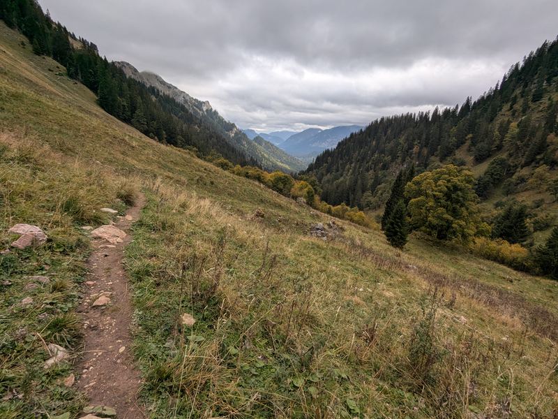 Ein schmaler Pfad quert einen Grashang oberhalb des Tals