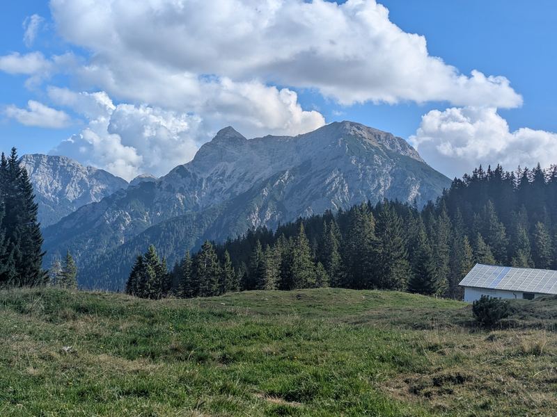 Eine Hütte am Rand der Almwiese, dahinter ein felsiger Gipfel