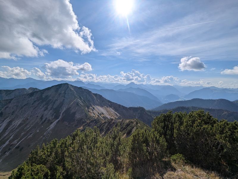 Gegenlicht über dem Gipfelgrat, in der Ferne gestaffelte Bergketten