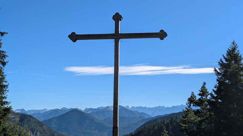 Das Gipfelkreuz auf dem Rabenkopf, dahinter die Berge des Isarwinkels